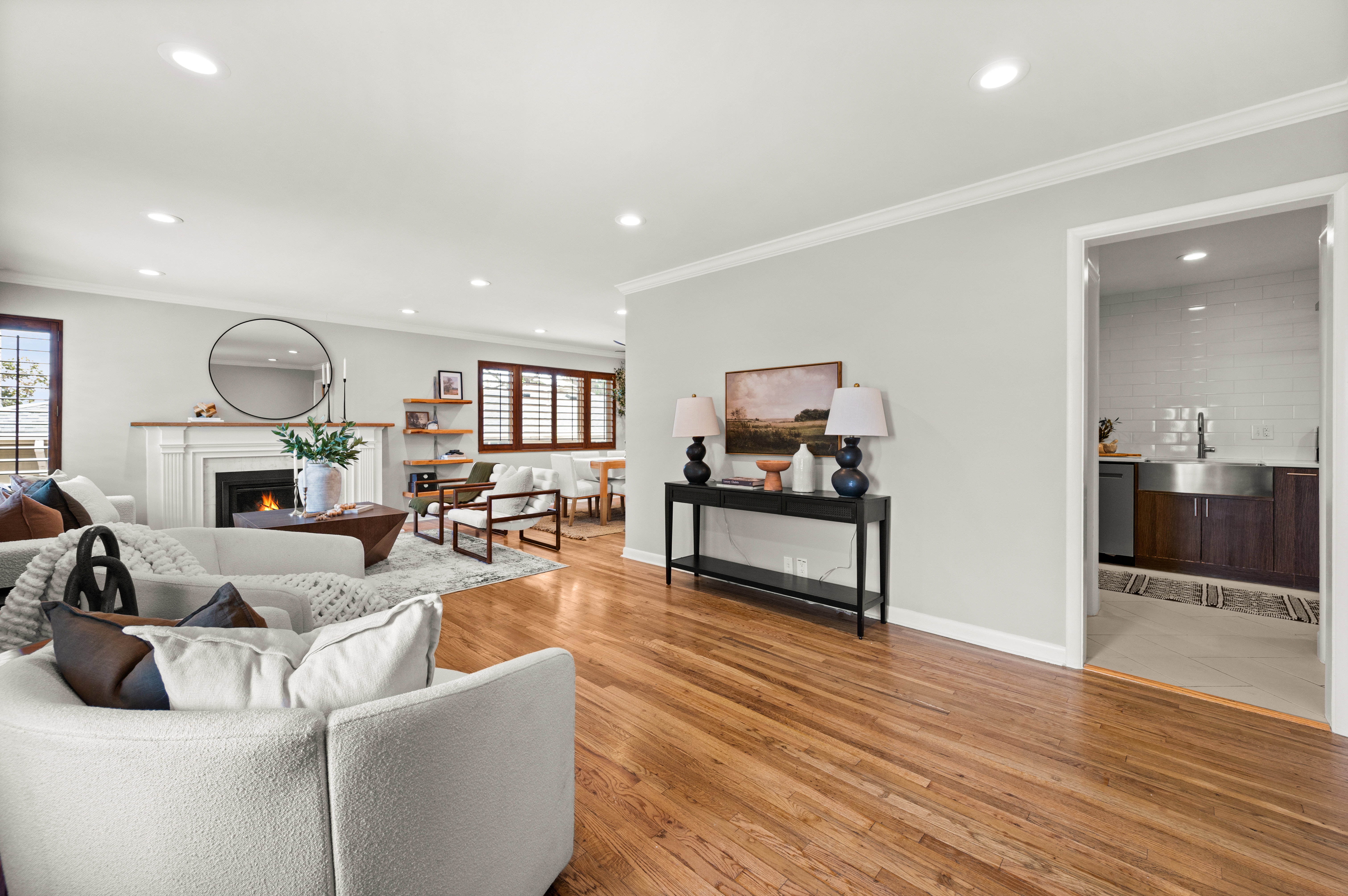 Spacious living area featuring polished wood-finish flooring, a white mantel fireplace, recessed lighting, and crown molding