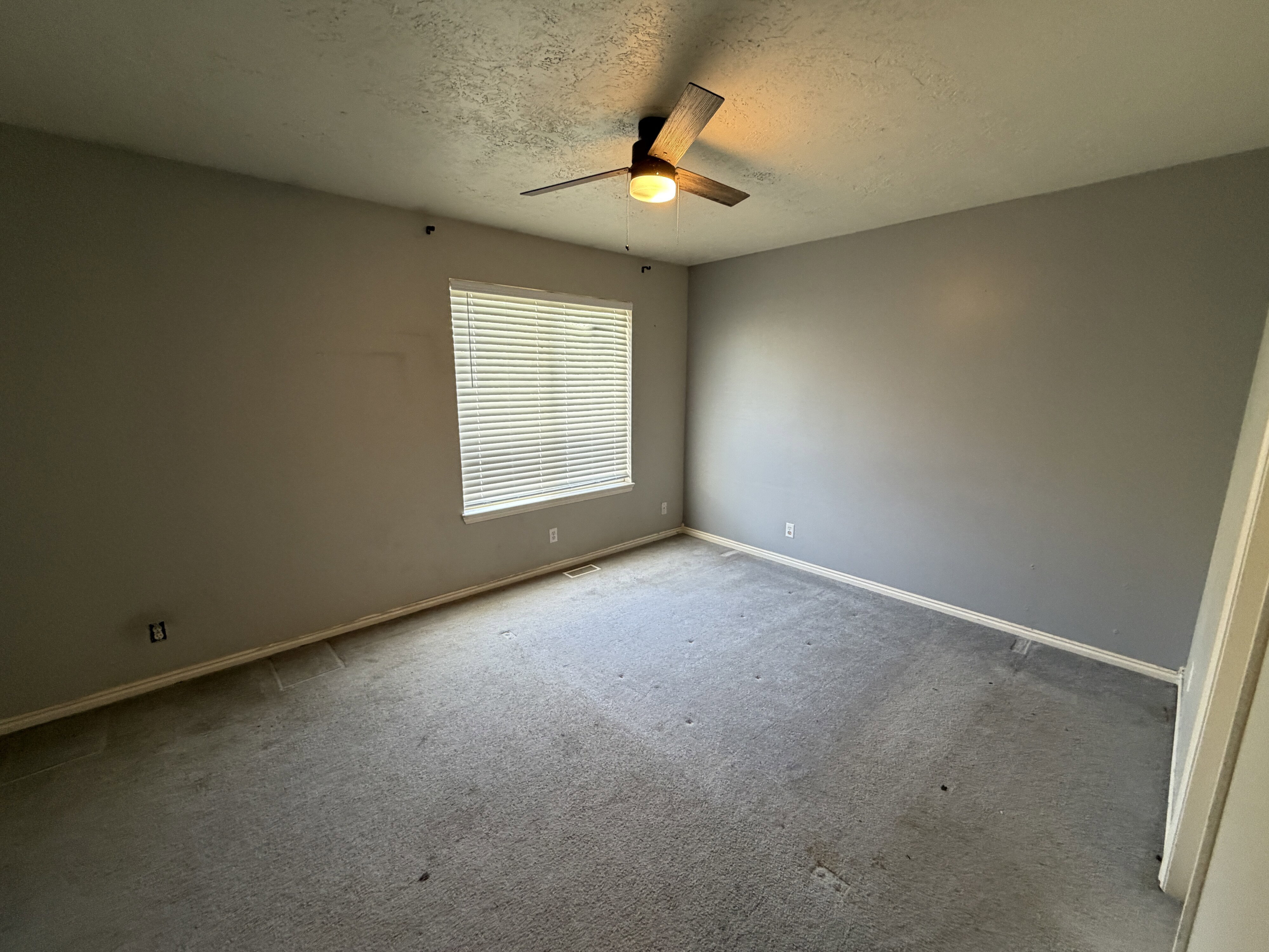 Interior room featuring neutral gray wall paint, a window with horizontal blinds, and a ceiling fan with integrated lighting
