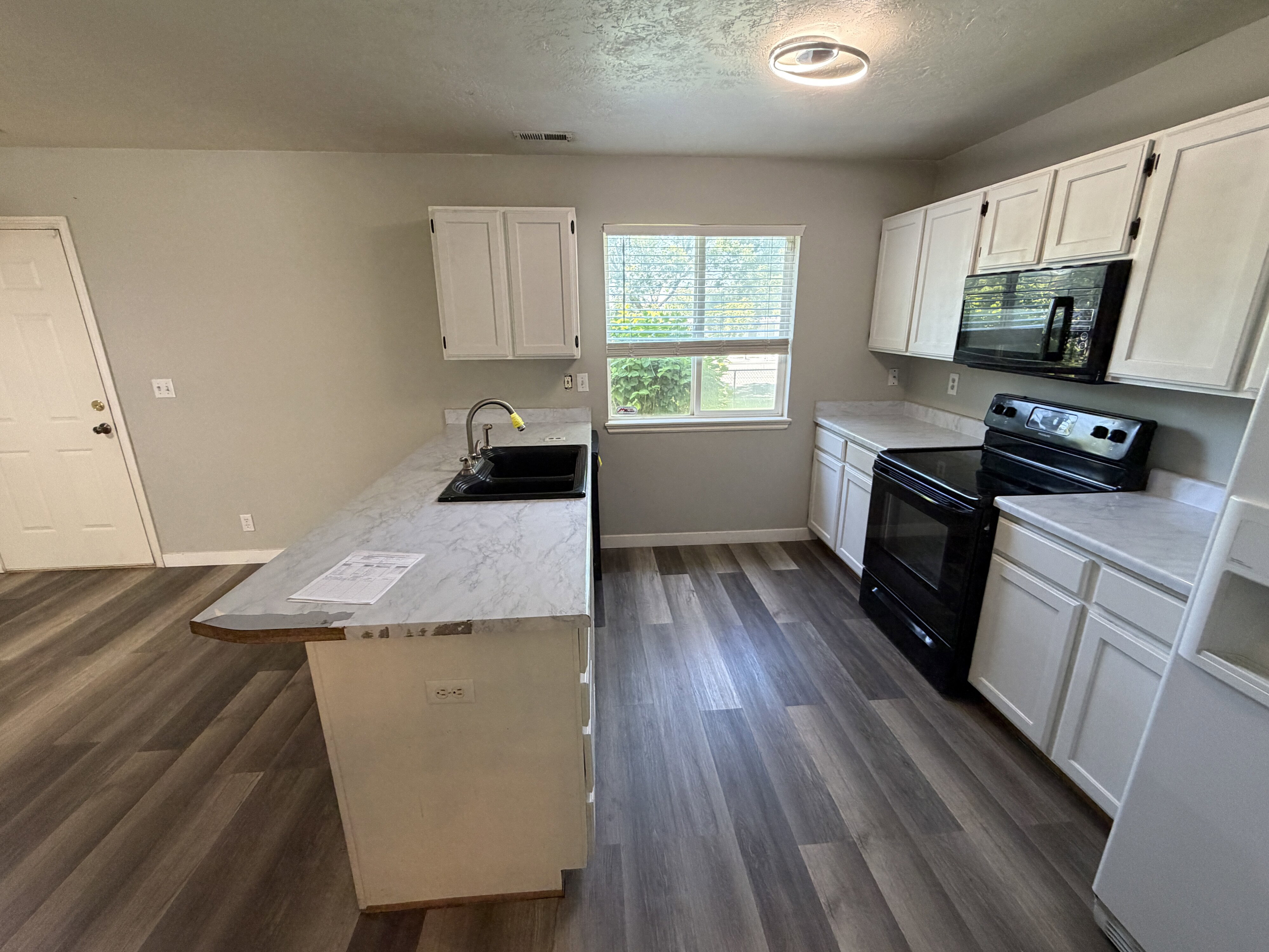 Kitchen featuring wood-finish flooring, white cabinetry, dark countertops, a black electric range, and an over-range microwave