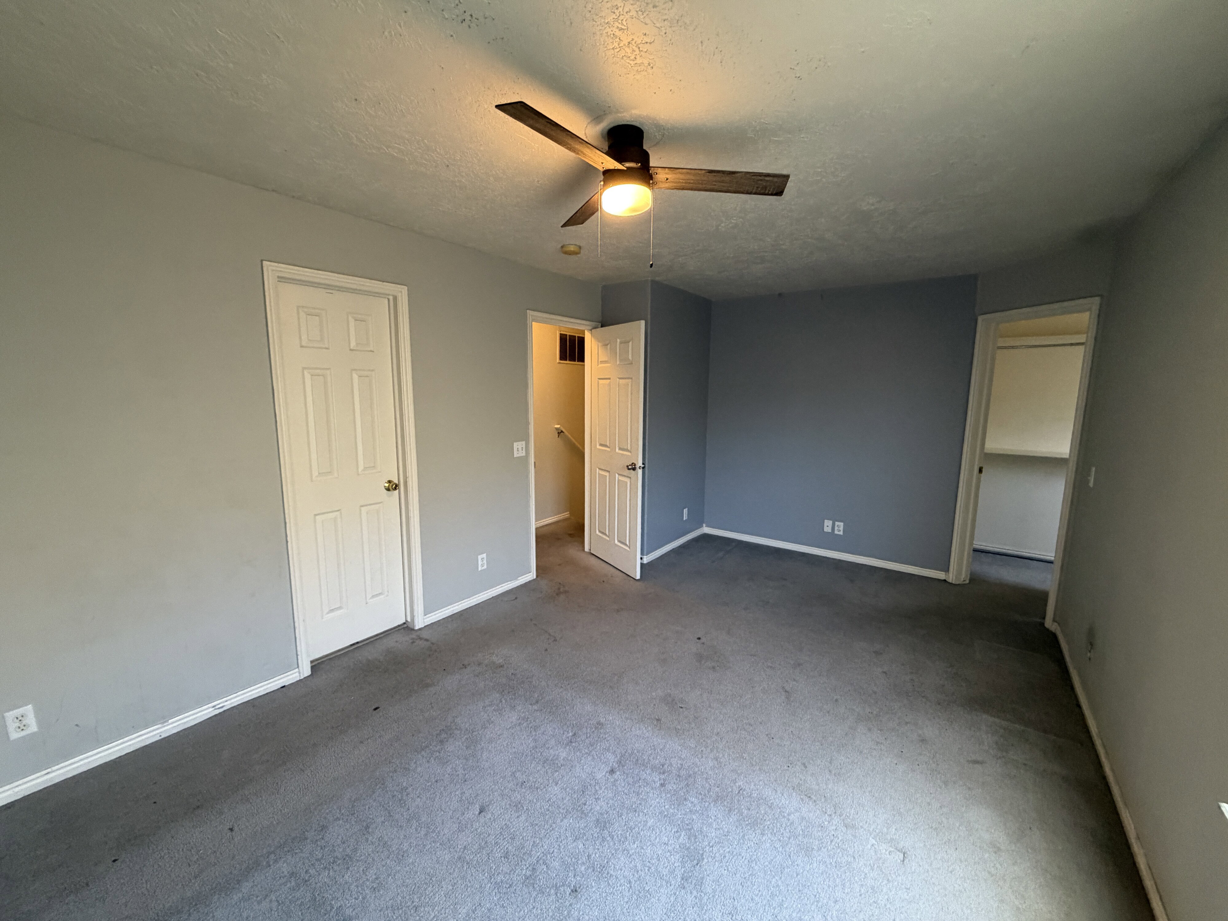 Spacious room featuring a ceiling fan with light fixture, neutral gray walls, and base molding