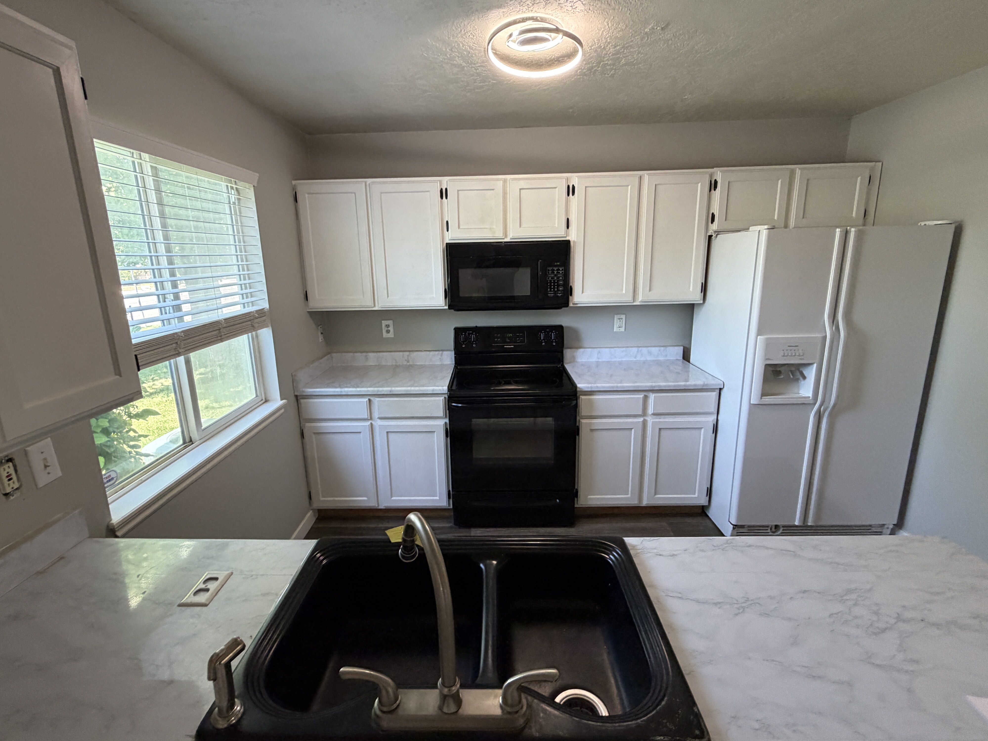 Kitchen featuring white cabinetry, integrated black appliances, a white refrigerator, and a double basin sink with a brushed metal faucet