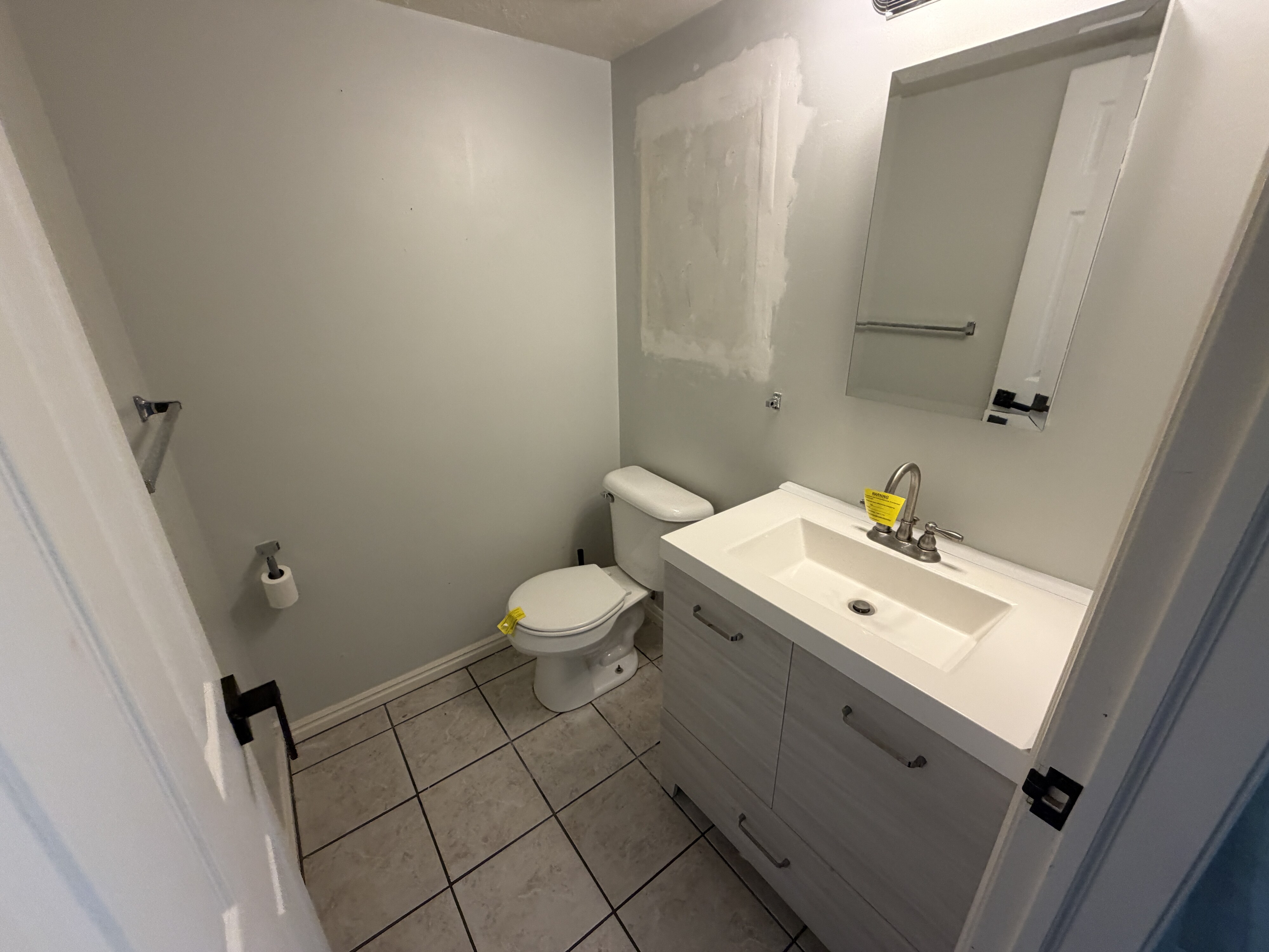 Bathroom featuring a light-toned vanity with integrated sink, brushed nickel faucet, large wall mirror, and square floor tiles