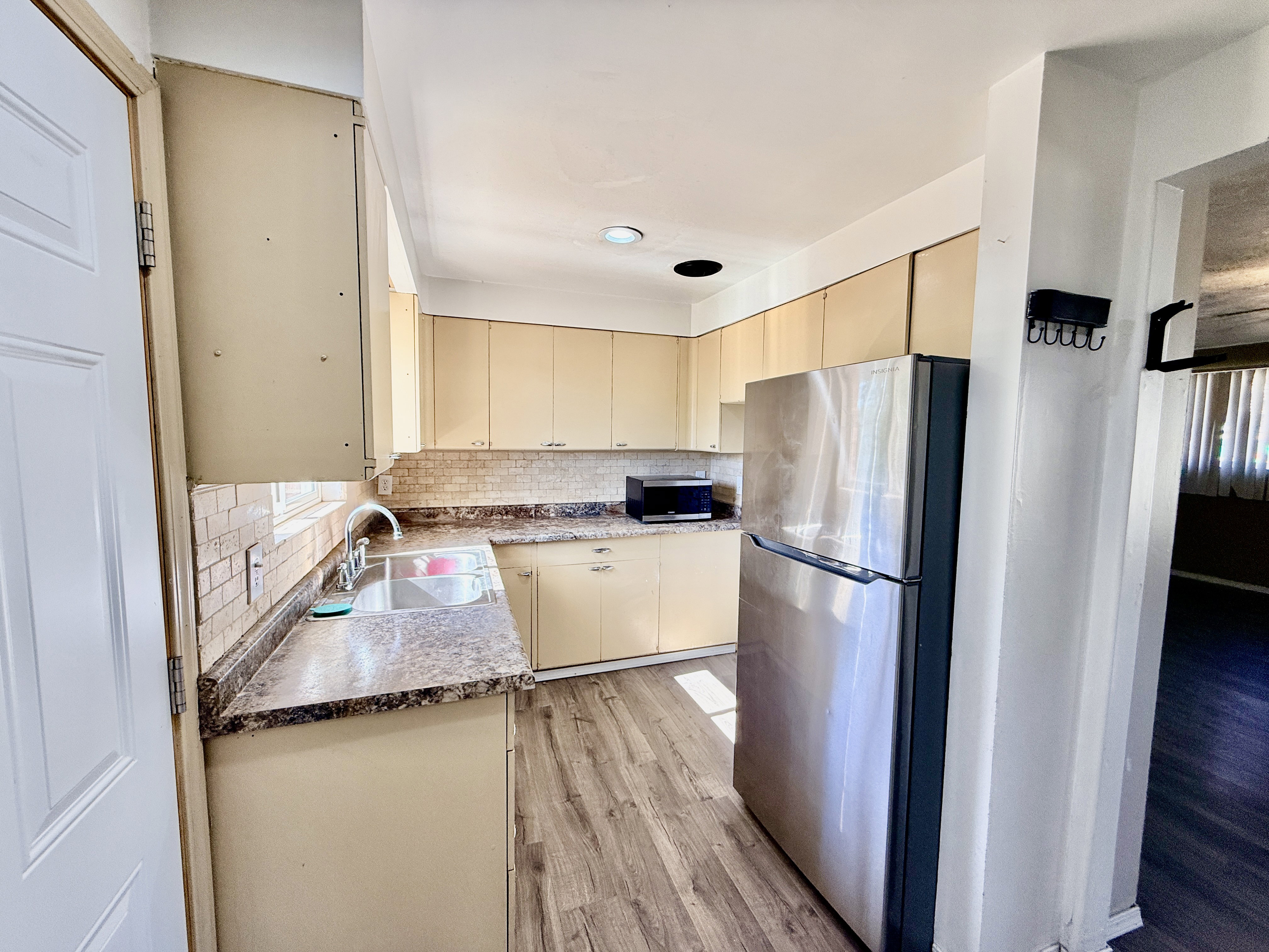 Kitchen featuring wood-finish flooring, light-toned cabinetry, stainless steel refrigerator, patterned countertops, and a tiled backsplash