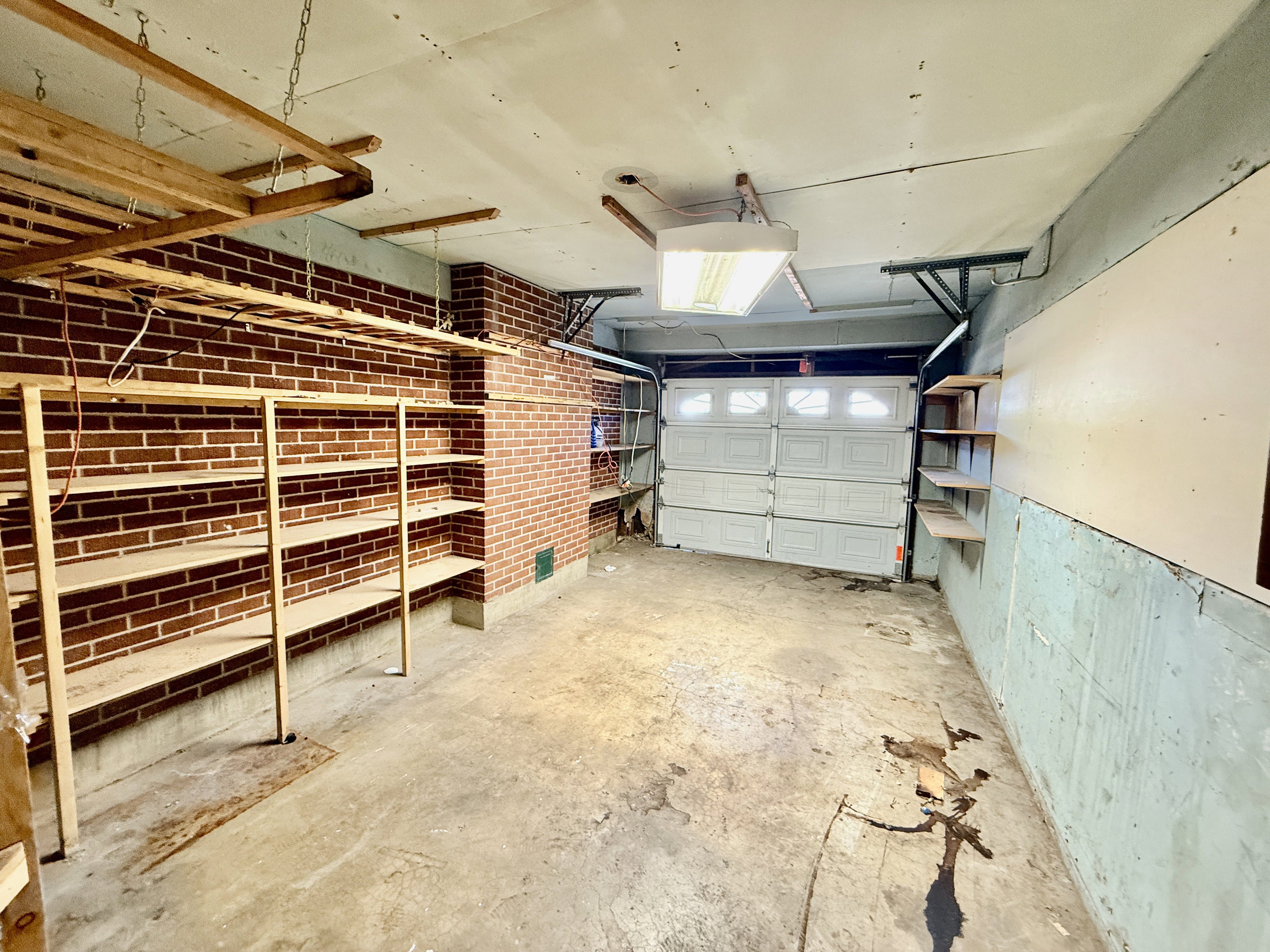 Garage interior featuring a sectional garage door, exposed brick wall, concrete flooring, and built-in shelving units