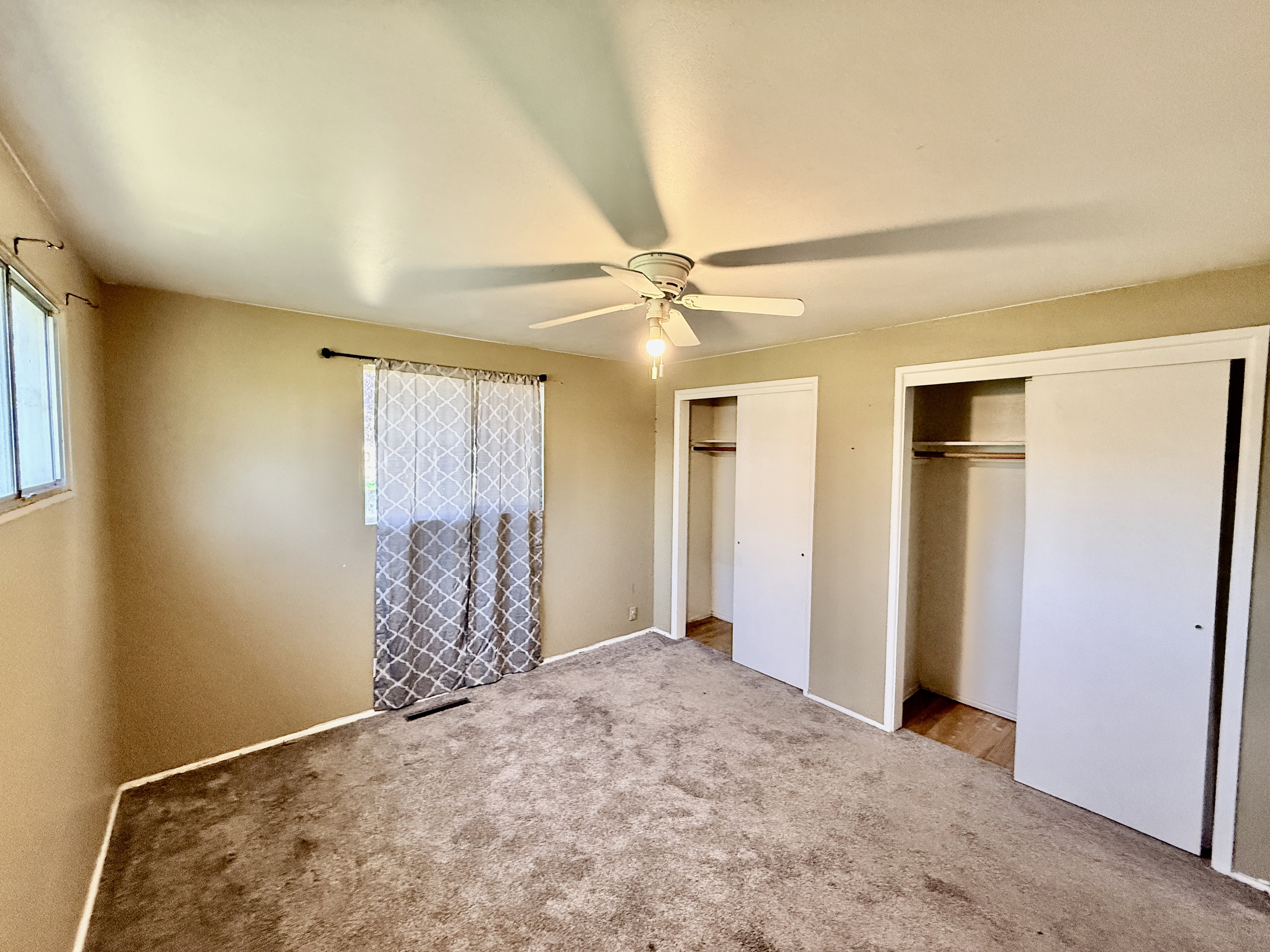 Carpeted room featuring a ceiling fan with integrated lighting, two windows, and two sliding door closets with interior shelving and hanging rods