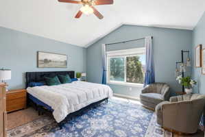 Vaulted ceiling bedroom with a large window and ceiling fan