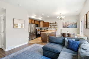 Open-concept living space featuring wood-finish flooring, a kitchen with wood cabinetry and stainless steel appliances, a breakfast bar, and a dining area with a contemporary chandelier