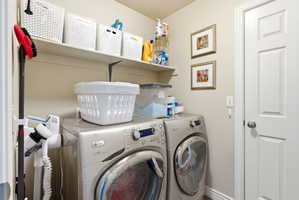 Dedicated laundry area featuring a front-loading washer and dryer set, wall-mounted shelving, and a paneled interior door