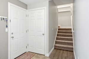 Entryway featuring two white panel doors, wood-finish flooring, and a carpeted staircase with white railing