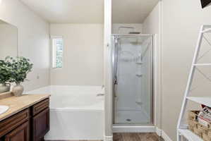 Bathroom featuring an inset bathtub with a window above, a separate glass-enclosed shower, a vanity with a light-colored countertop, and wood-finish flooring