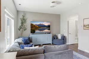 Spacious living area featuring light gray walls, wood-finish flooring, and a sliding glass door with blinds