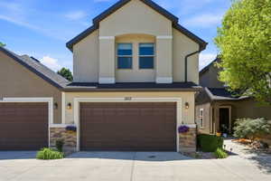 Stucco exterior with stone accent detailing, dual garage doors, and exterior lighting fixtures