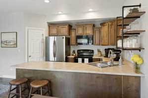 Kitchen featuring a breakfast bar with seating, wood-finish cabinetry, stainless steel appliances, and open shelving with industrial-style piping