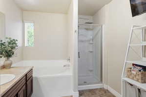 Bathroom featuring a white soaking tub, an enclosed shower with a rainfall showerhead, and a vanity with a light-colored countertop