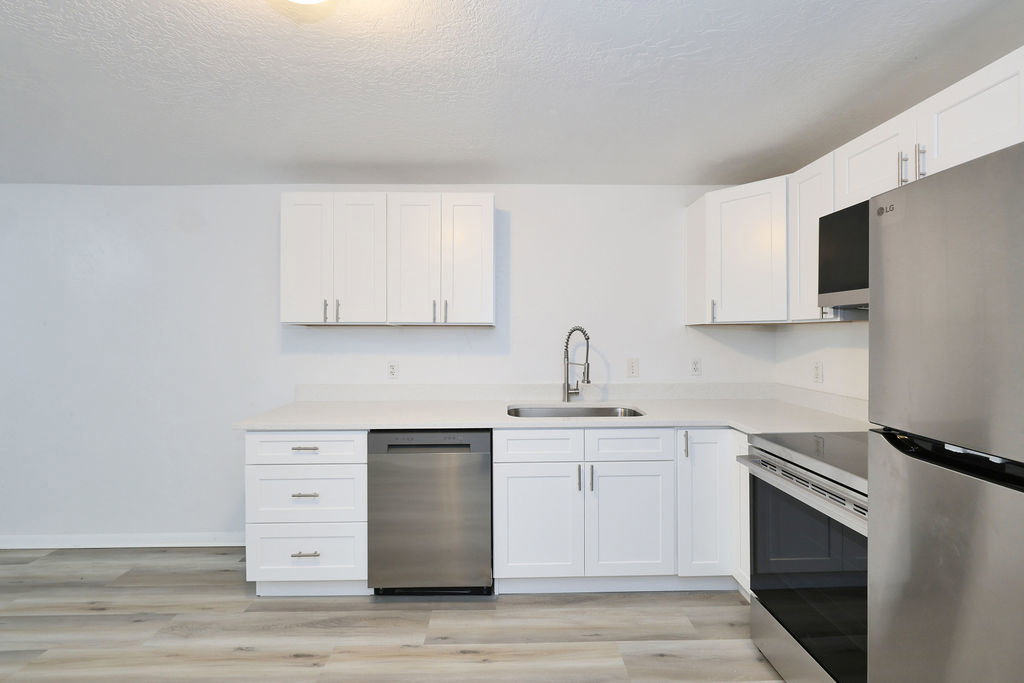 Modern kitchen featuring white shaker cabinetry, stainless steel appliances, light-toned countertops, and wood-finish flooring
