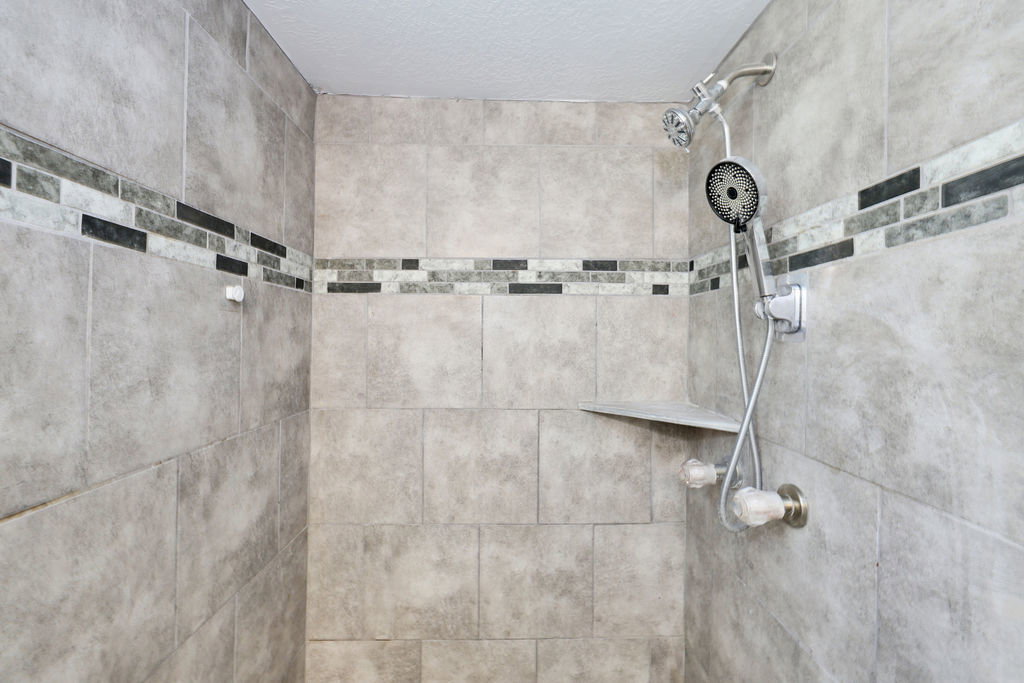 Tiled shower enclosure featuring light grey rectangular tiles with a decorative mosaic band