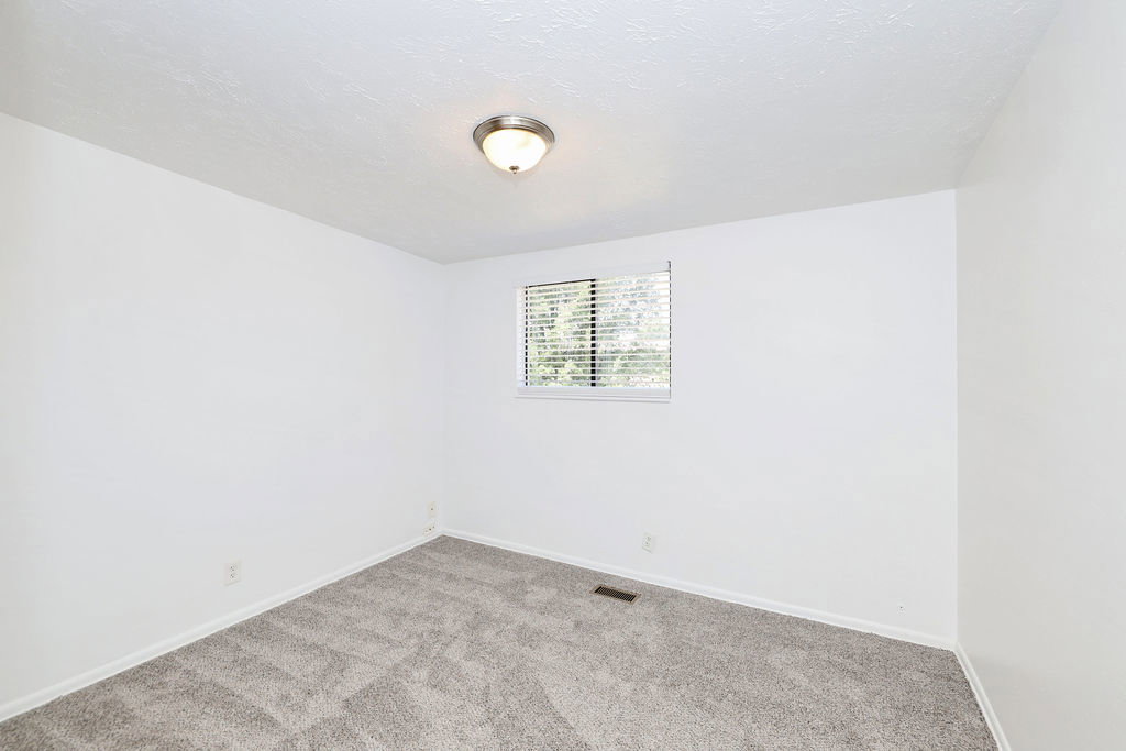 Room featuring light gray carpet, white walls, a flush-mount ceiling light fixture, and a window with blinds