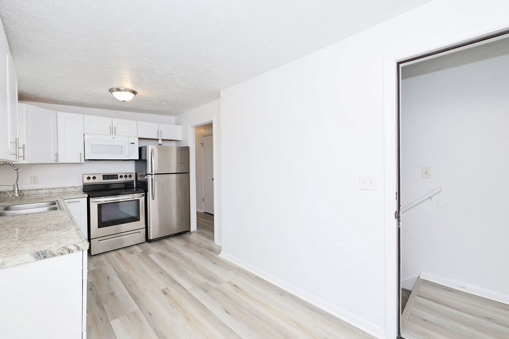 Modern kitchen featuring white cabinetry, stainless steel appliances, light-toned countertops, a stainless steel sink with a gooseneck faucet, and wood-finish flooring