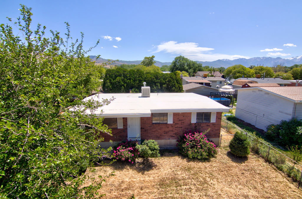 Brick exterior with white trim, featuring a flat roof and surrounding established landscaping