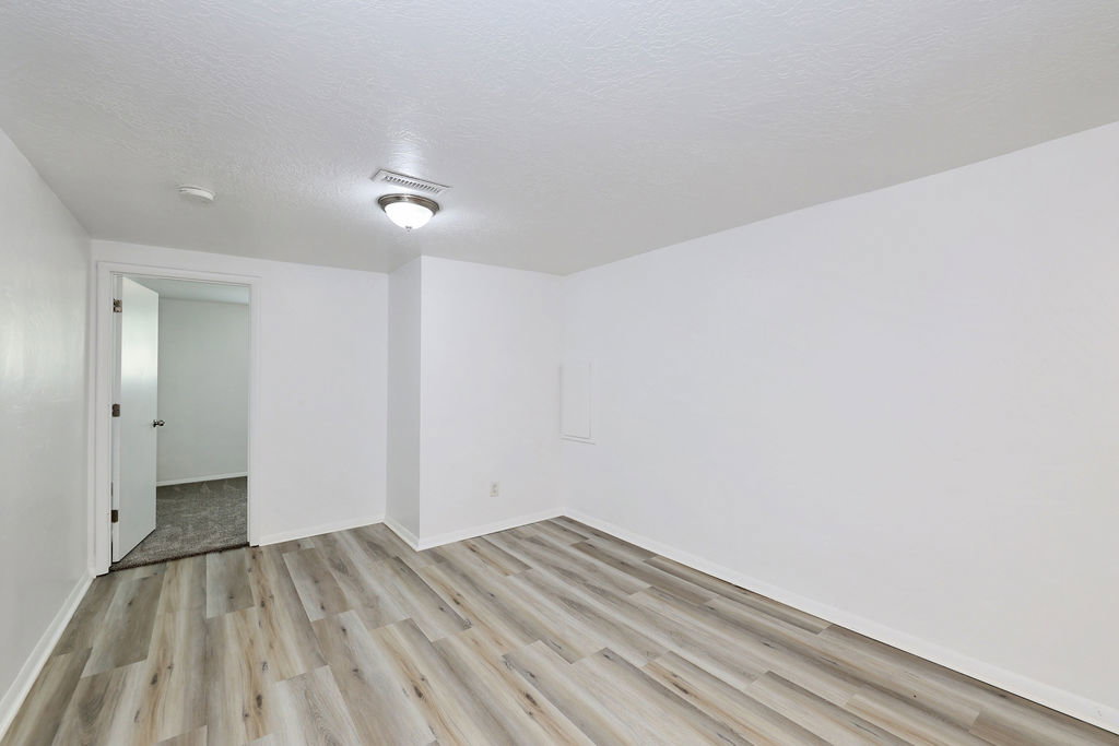 Spacious interior room featuring wood-finish flooring, white walls, and a recessed ceiling light fixture