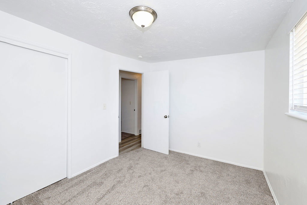 Carpeted interior room featuring a window with blinds, a white door, a closet with sliding doors, and an overhead flush mount light fixture