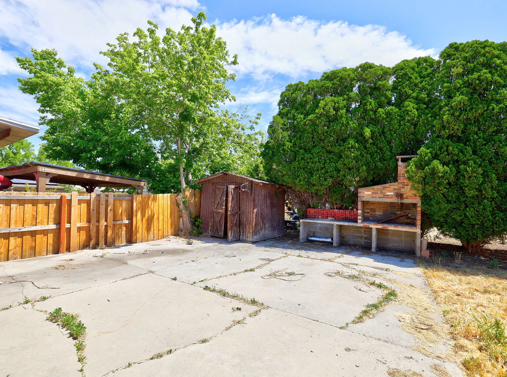 Concrete patio area featuring a built-in brick BBQ, a detached storage shed, and a wooden privacy fence
