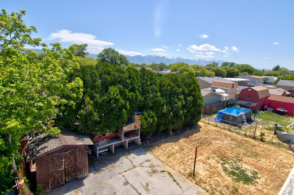 Expansive outdoor space featuring mature trees, a wooden storage shed, and a built-in brick barbecue station