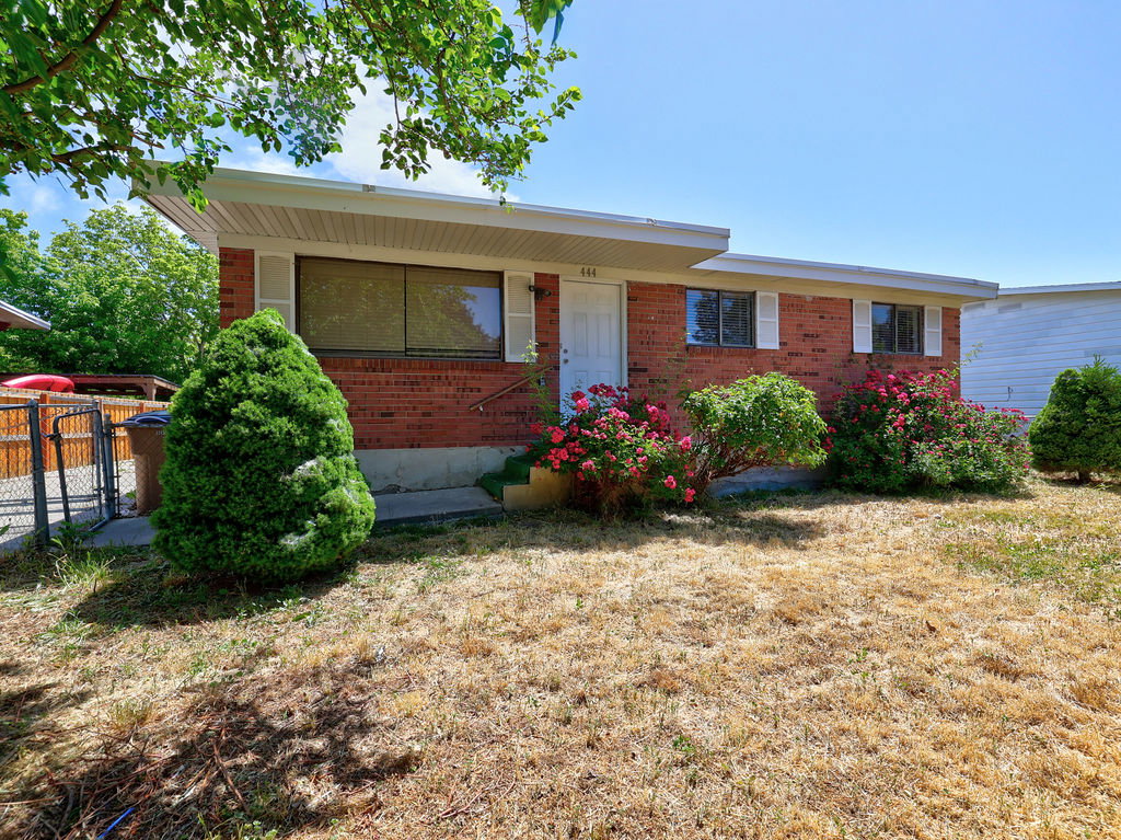 Brick exterior featuring white window shutters, mature shrubbery, and a front entry door with a privacy screen