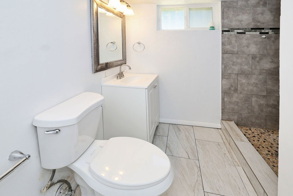 Full bathroom featuring a white vanity with integrated sink, a rectangular mirror, a shower with stone tile surround and pebble floor, and light-toned tile flooring