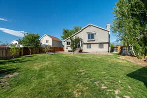 Expansive rear yard featuring a large grass lawn, mature trees, wood fencing, a concrete patio, and a light-colored exterior with multiple windows