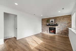 Living area featuring a brick accent wall with a fireplace and mantel, wood-finish flooring, recessed lighting, and a white baseboard and trim package