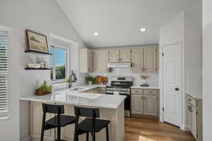 Kitchen featuring an angled ceiling, recessed lighting, wood-finish flooring, white subway tile backsplash, and stainless steel appliances