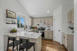 Light-filled kitchen featuring vaulted ceilings, white subway tile backsplash, light wood-finish flooring, and a window above the sink