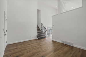 Two-story entry foyer featuring wood-finish flooring, a carpeted staircase with black metal railings, and vaulted ceilings with recessed lighting