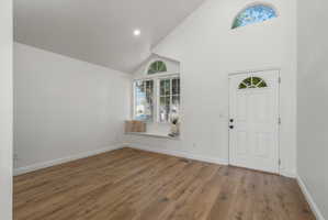 Vaulted ceiling entry featuring a window seat, wood-finish flooring, and white paneled door with an arched transom window