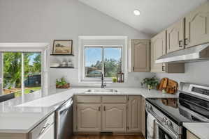 Kitchen featuring vaulted ceilings, light-colored cabinetry, stainless steel appliances, white countertops, and a subway tile backsplash