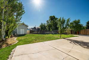 Patio Expansive backyard featuring a large concrete patio, a detached storage shed, mature trees, a wooden perimeter fence, and a manicured lawn