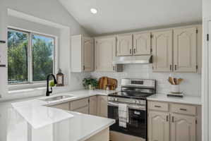 Kitchen featuring white subway tile backsplash, light-colored cabinetry with dark hardware, stainless steel range and range hood, and white countertops