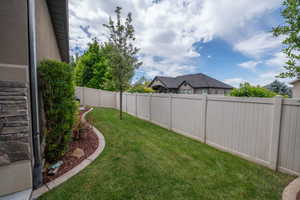Private side yard with lush green lawn, manicured planting beds, mature trees, and full vinyl privacy fencing. Clean, tidy, and easy to maintain.