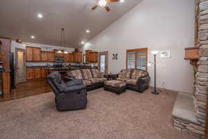 Wide angle view captures the full open-concept layout, with vaulted ceilings, the stone fireplace anchoring the living space, and the knotty alder kitchen flowing seamlessly behind. Ceiling fan, recessed lighting, and abundant natural light throughout.