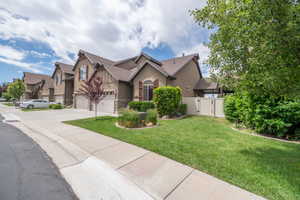 Wide angle street view captures the full footprint of the home, lush front lawn, vinyl privacy fence gate, and mature tree canopy framing the property. Great end presence.