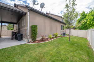 Back of the home shows stucco and stacked stone exterior, covered patio, landscaped yard, and vinyl privacy fence. Low-maintenance and well-kept.