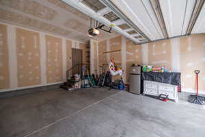 Second look at the spacious two-car garage showing the full depth, drywalled walls, automatic opener, built-in shelving, and direct interior access via staircase entry.