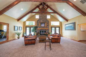 Stunning clubhouse great room with soaring vaulted ceilings, dramatic exposed wood beam trusses, floor-to-ceiling stacked stone fireplace, and French doors opening to the pool area. The fitness room is visible off to the side. This amenity space is except