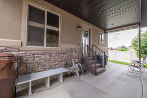 Covered patio entry with stacked stone exterior detail, iron railing staircase, wall sconce lighting, and a finished patio ceiling. Solid craftsmanship inside and out.