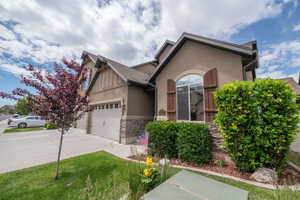 Charming front elevation angle highlighting the craftsman roofline, board-and-batten siding, wood shutters, ornamental plum tree, and stacked stone base. This home photographs beautifully from every angle.