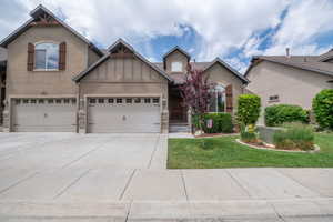 Beautiful daytime curb appeal showcasing craftsman-style architecture, 2-car garage, stacked stone accents, board-and-batten details, ornamental tree, and lush manicured landscaping.