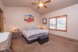 Generously sized primary suite with vaulted ceilings, ceiling fan, plush carpet, and a large wood-trimmed window. Bright, airy, and made for rest.