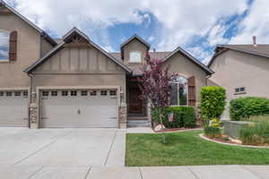 Closer look at the front entry, highlighting the warm wood front door, arched windows, stacked stone columns, and thoughtfully planted flower beds. Solid, stunning craftsmanship from the street.