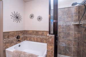 Closer look at the soaking tub and walk-in shower side by side, with beautiful stone-look tile, mosaic accent trim, and quality fixtures. A true spa-style setup.